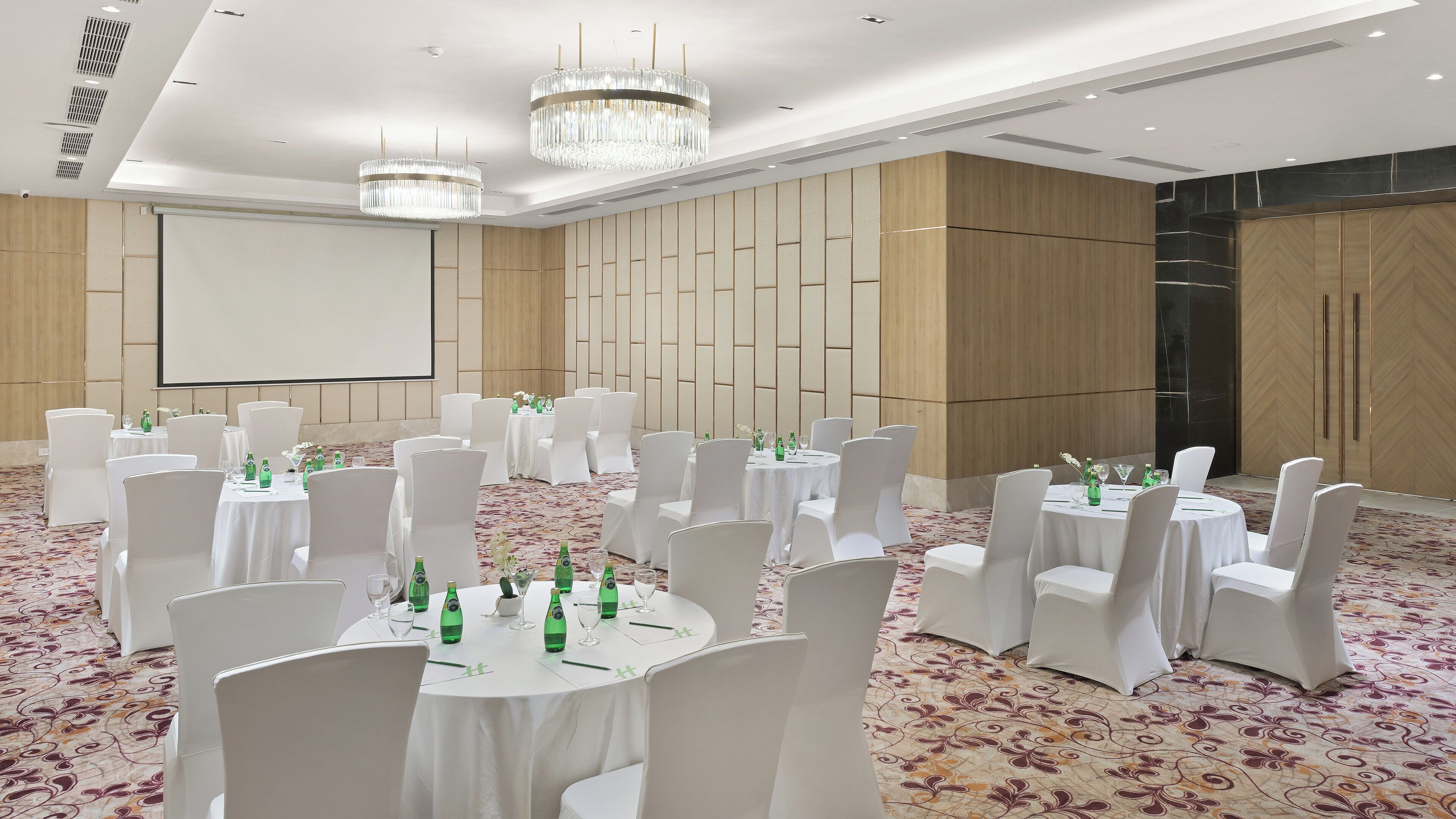 A conference room with round tables, white chairs, and chandeliers.