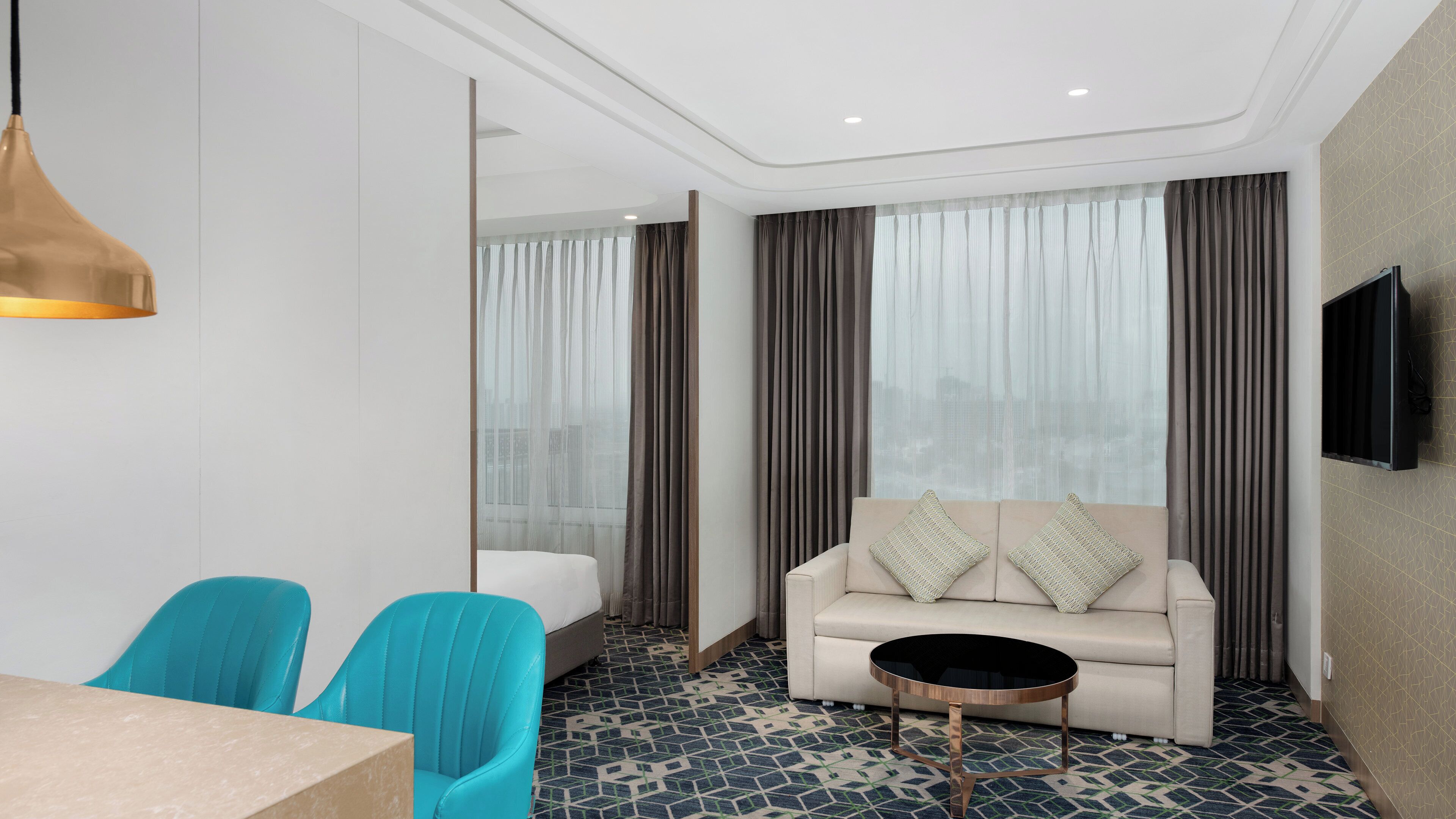 Une chambre d’hôtel moderne, équipée d’un canapé, de deux fauteuils, d’une télévision et d’un sol à motifs.