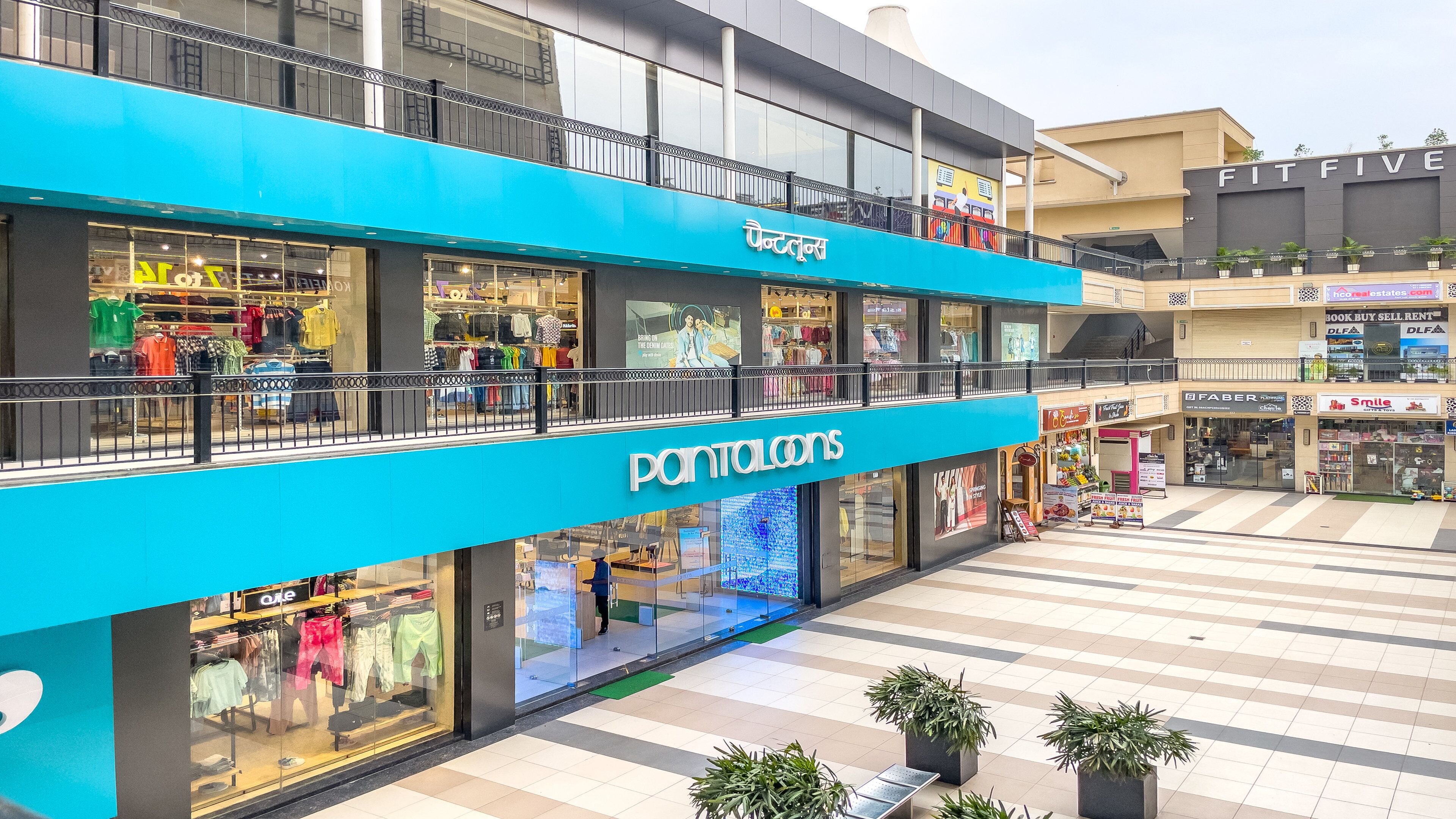 A multi-level shopping mall with stores like 'Pantalons' and 'FitFive'.