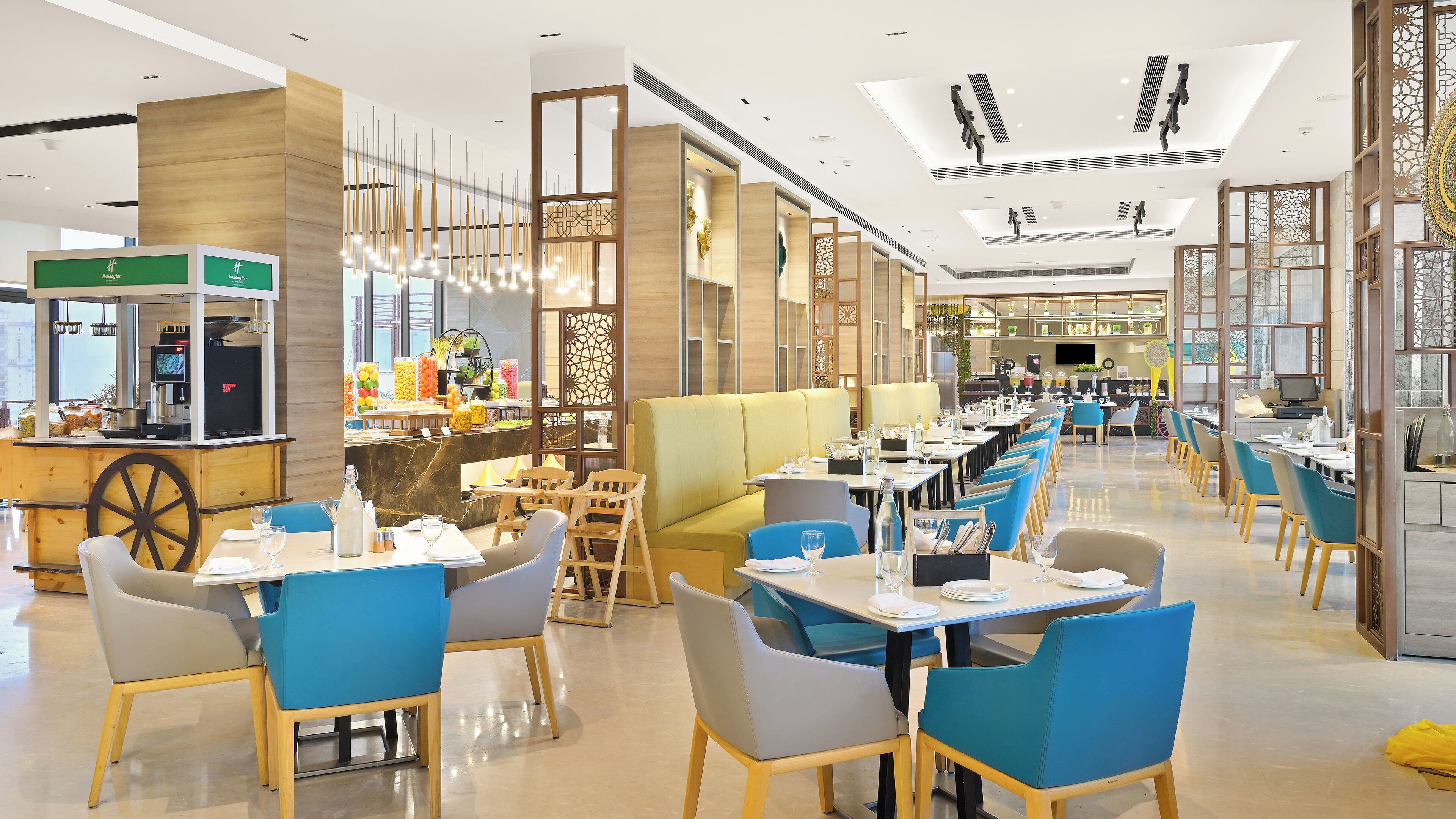 Un restaurant moderne avec un intérieur élégant, de hauts plafonds, un bar central et différents types de sièges, notamment des banquettes et des tables.