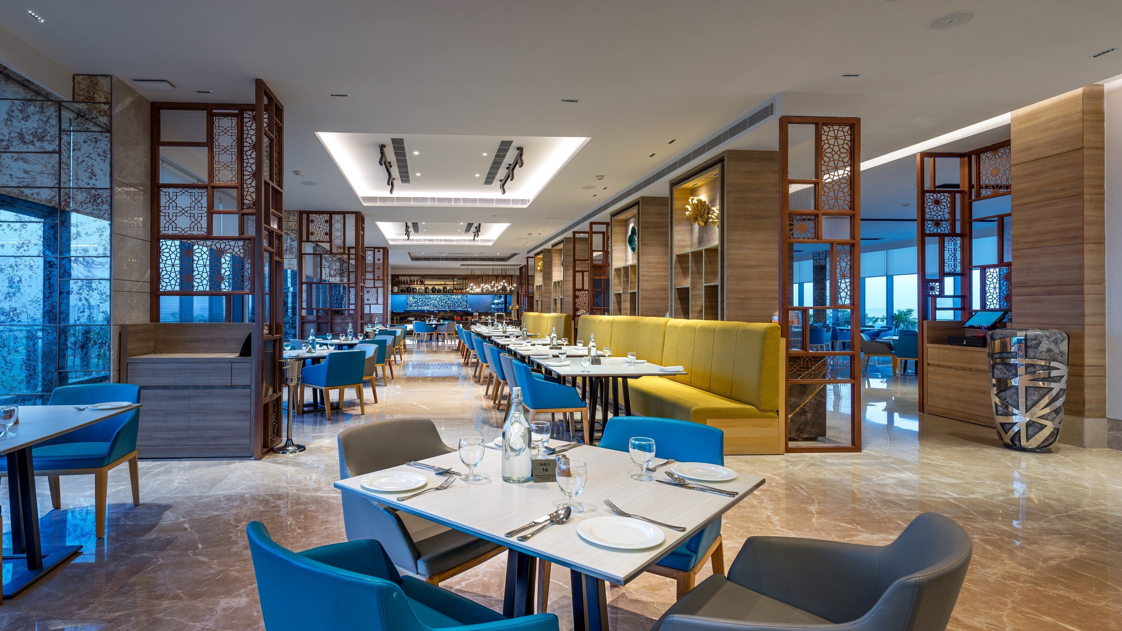 A modern restaurant with blue and yellow seating, a bar area, and decorative wooden partitions.