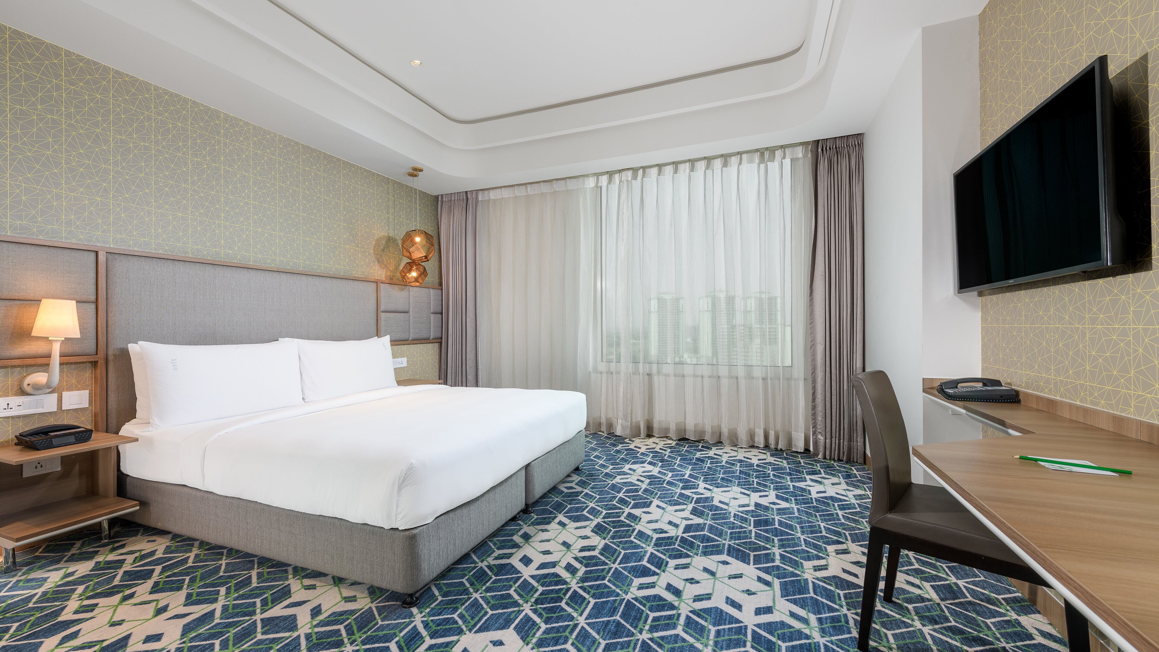 A hotel room with a bed, a desk, a chair, a TV, and a window with curtains.