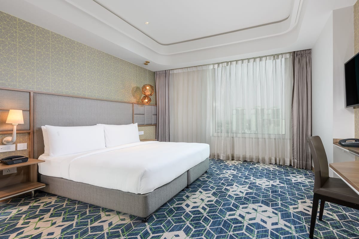 A hotel room with a bed, a desk, a chair, a TV, and a window with curtains.