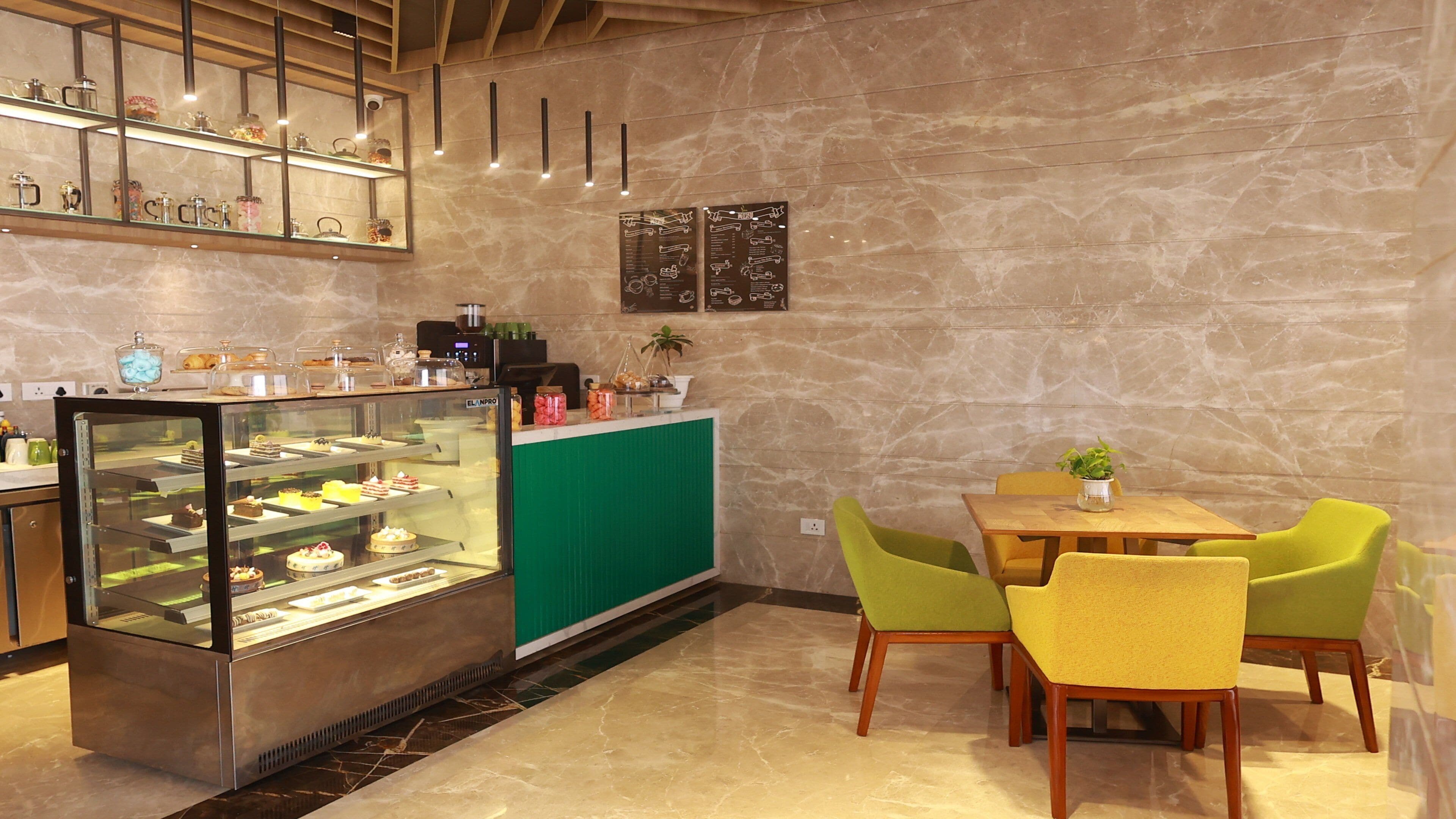 Un café avec une vitrine remplie de pâtisseries, un comptoir vert et des chaises jaunes.