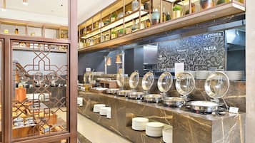 Un espace buffet doté de plusieurs points de service, d’une signalétique indiquant l’emplacement de la cuisine, et d’une variété d’aliments présentés sur des étagères.