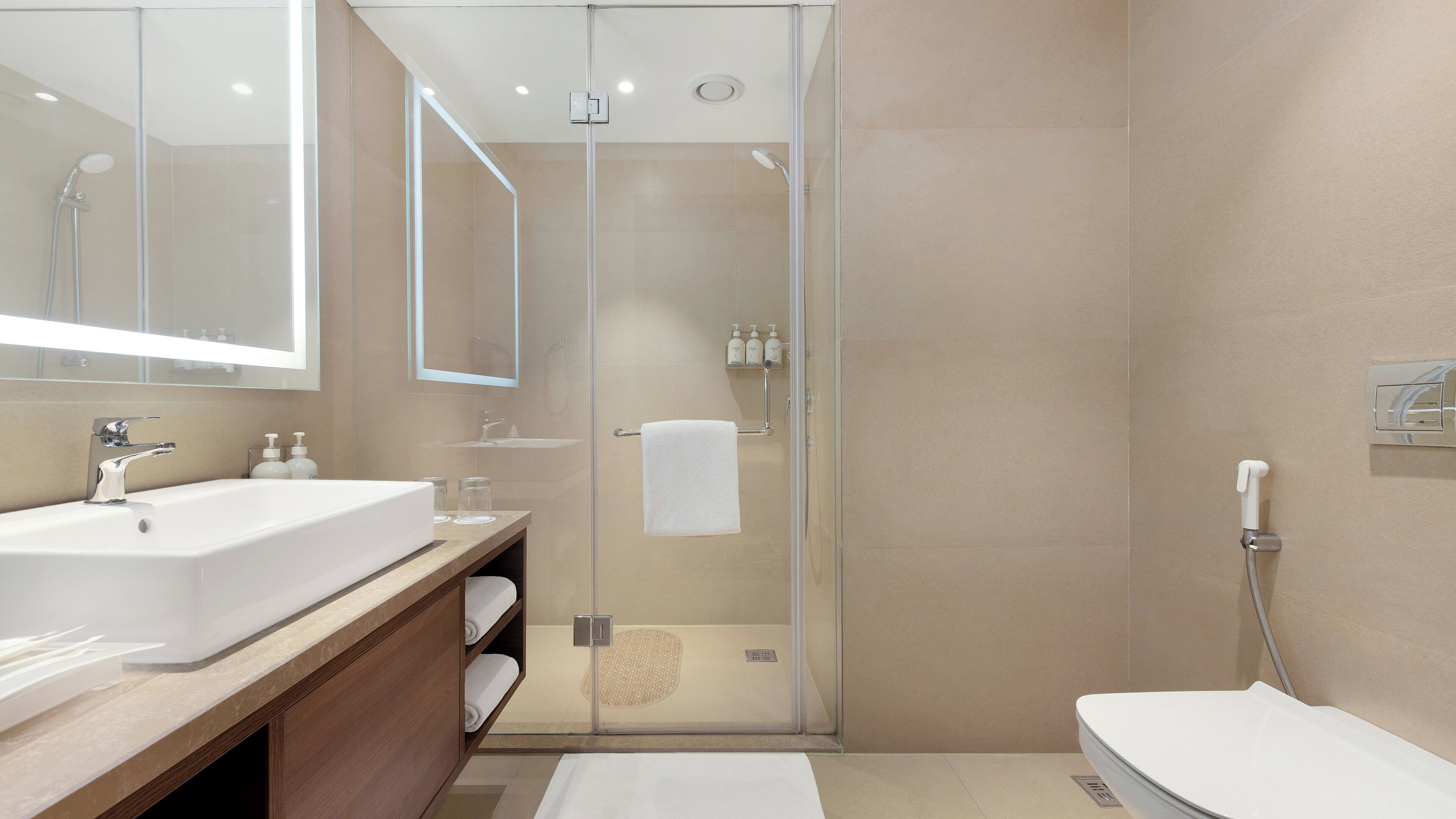 Ein modernes Badezimmer mit einer Glaskabine zur Dusche, einem großen Spiegel und einem weißen Waschbecken.