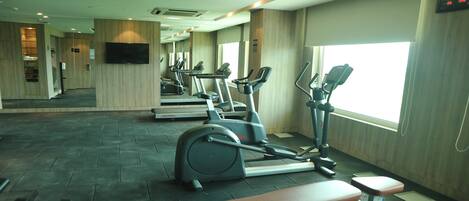 Un gimnasio con cintas de correr, elípticas y una banca.