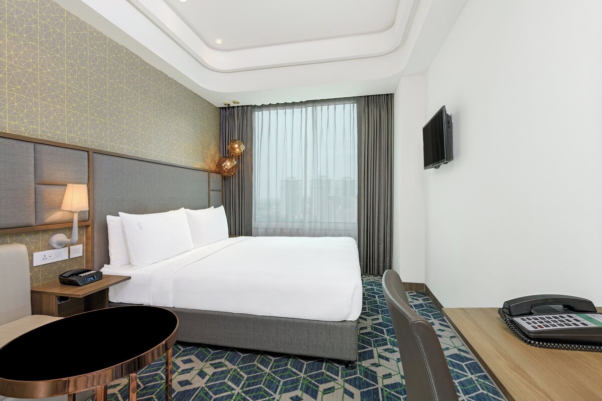 A hotel room with a bed, bedside table, lamp, and a phone on the side table.