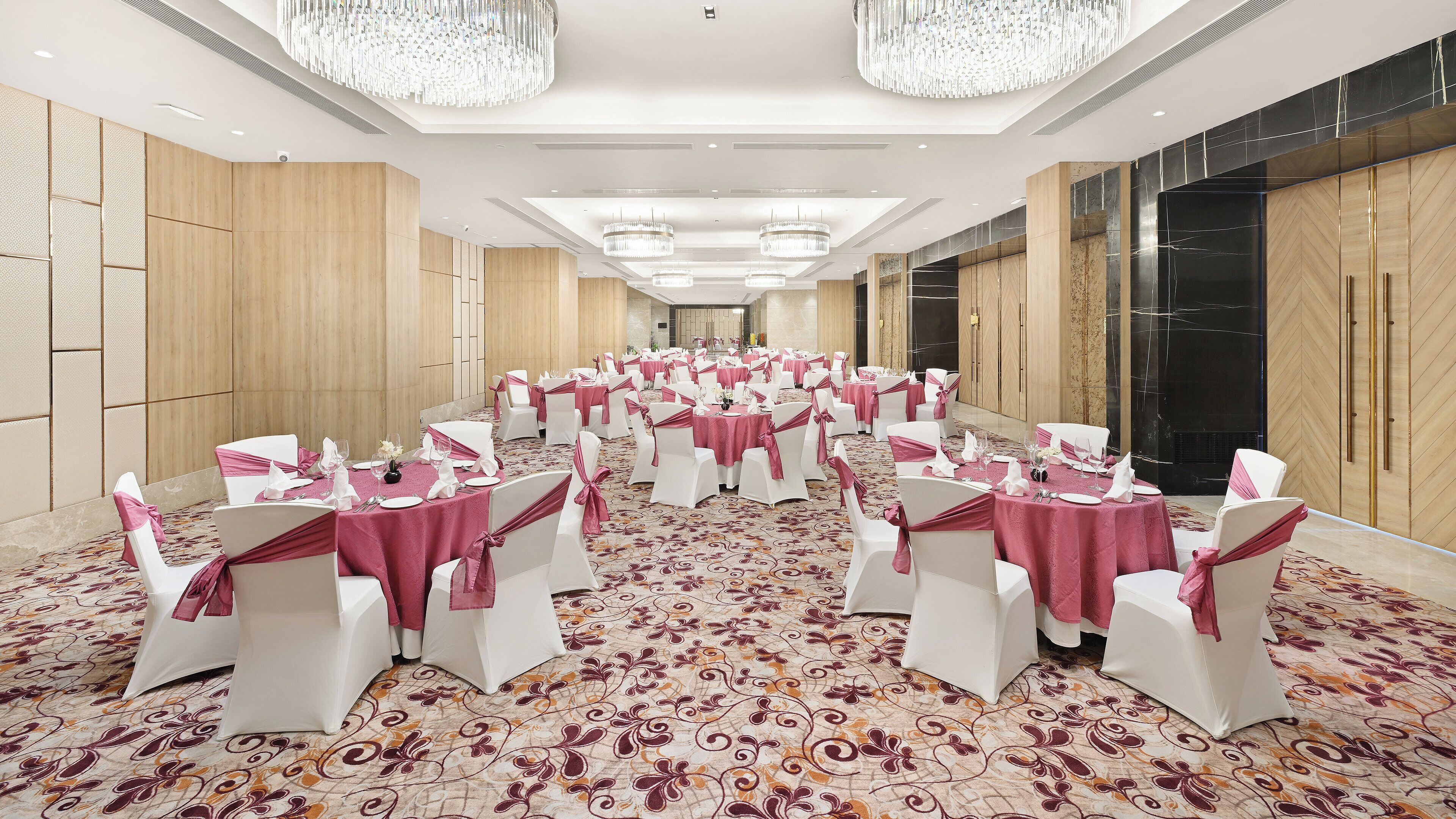 A banquet hall with round tables, white chairs, and pink tablecloths.