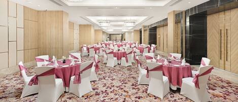 A banquet hall with round tables, white chairs, and pink tablecloths.