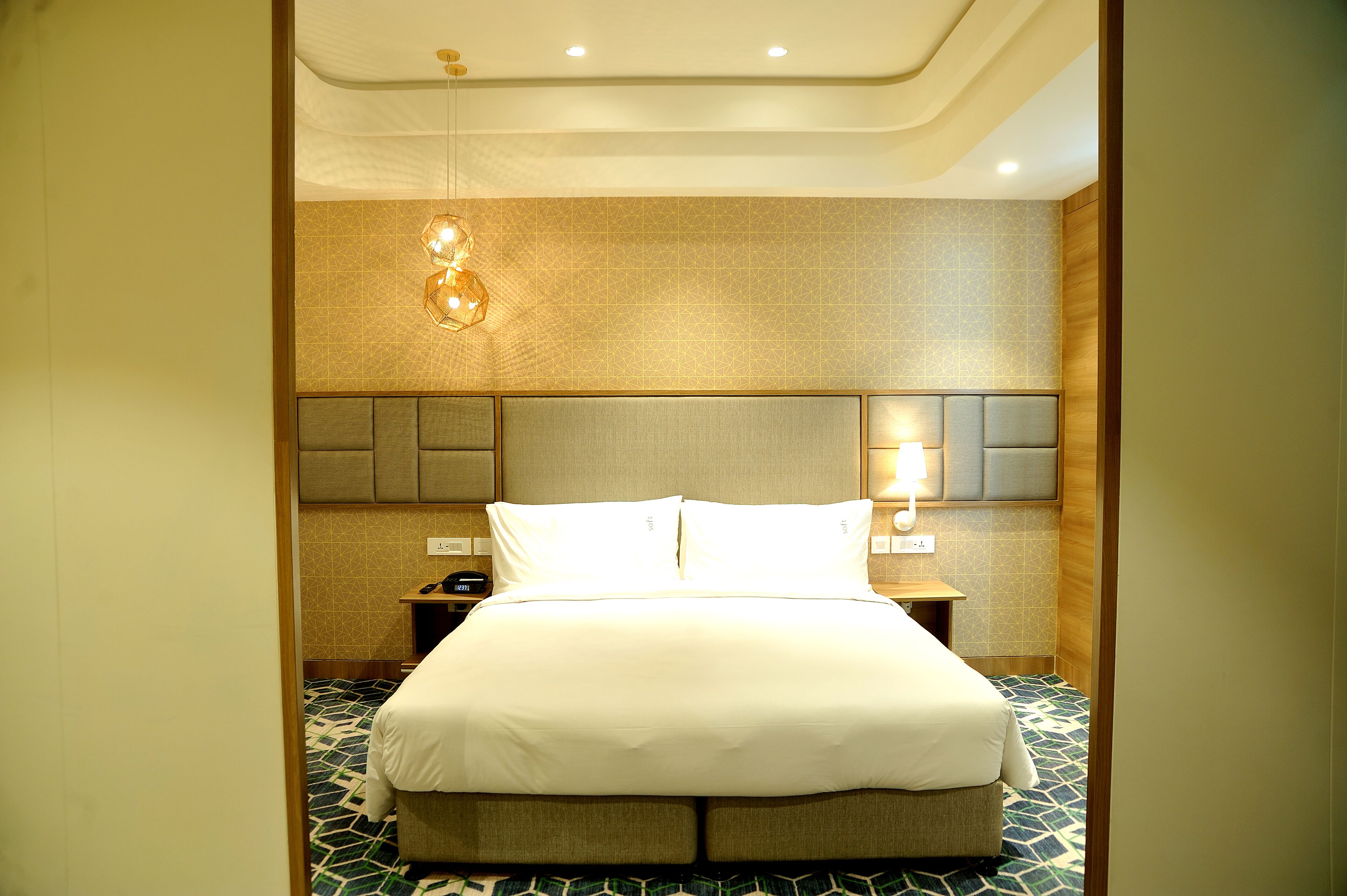 A hotel room with a large bed, a nightstand, a wall-mounted lamp, and a patterned floor.