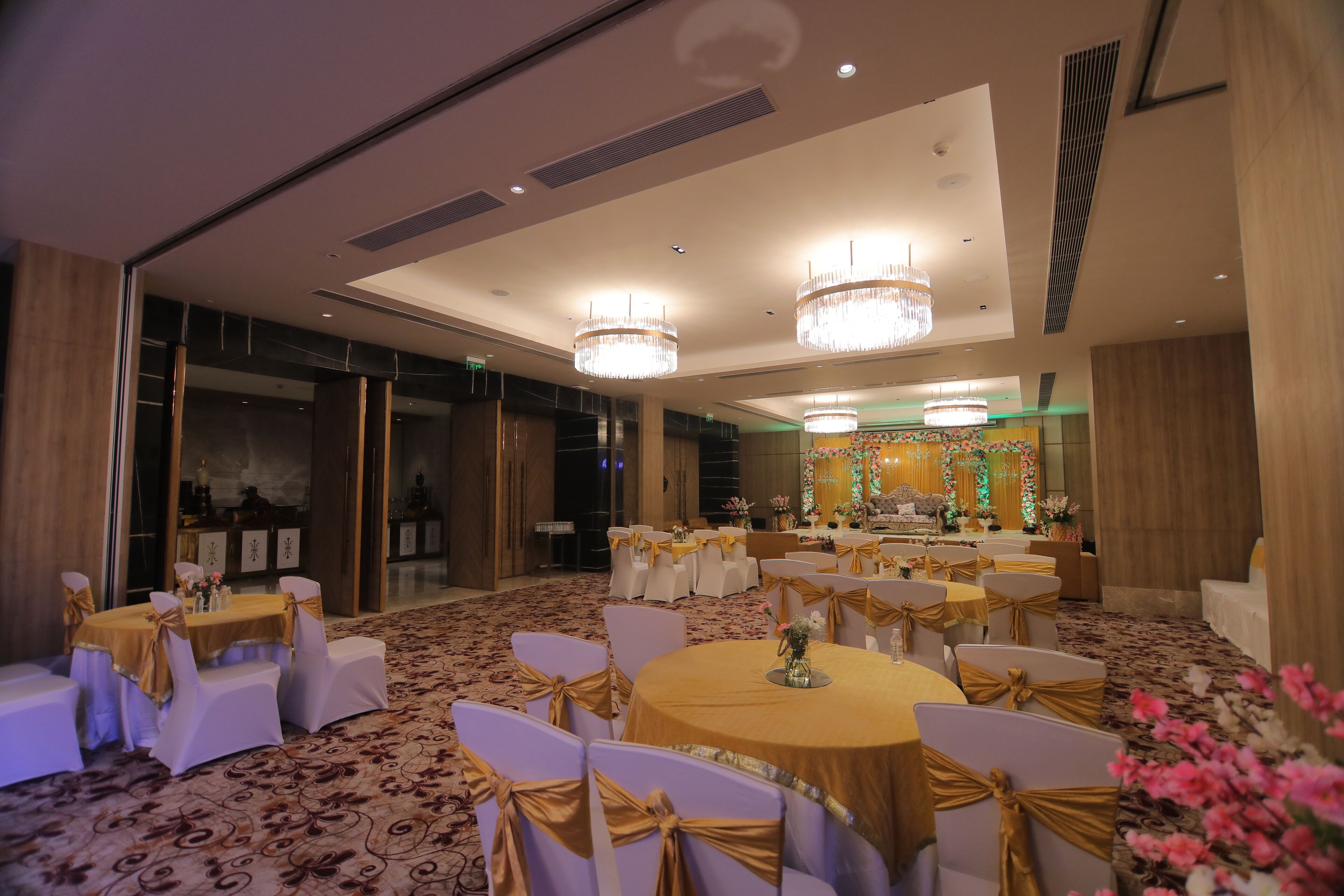 A banquet hall with round tables and white chairs, adorned with gold sashes.