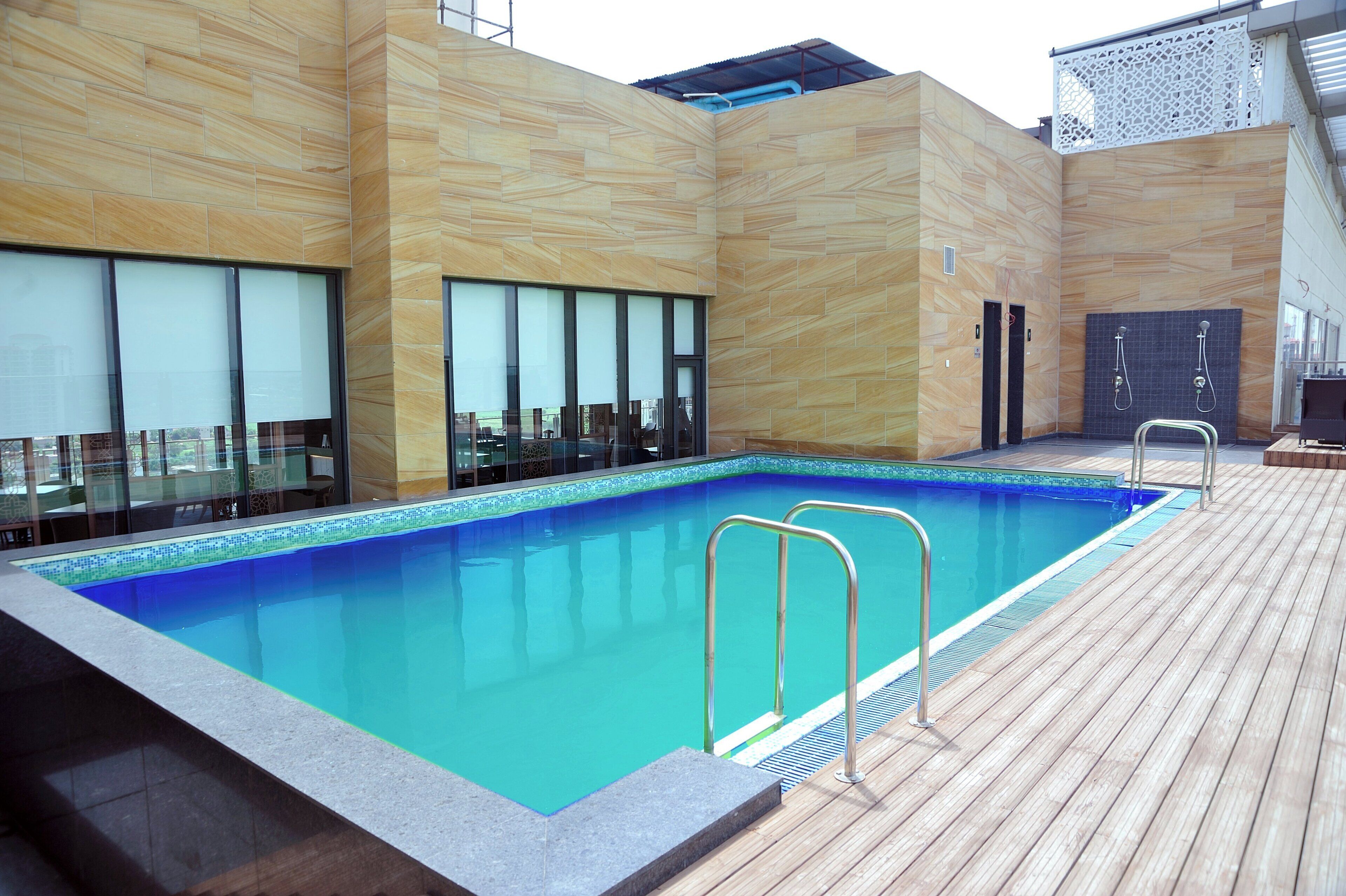 A swimming pool with a wooden deck, glass doors, and a tiled wall.