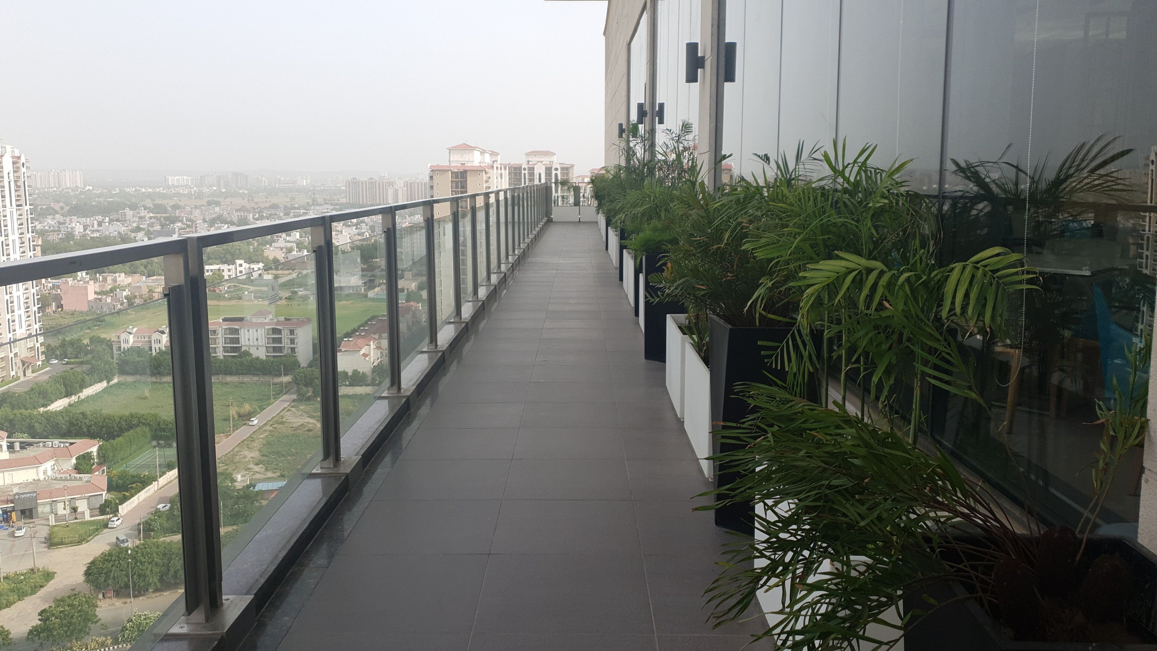 Ein Balkon mit Glasgeländer, der einen Blick auf eine Stadt mit modernen Gebäuden und Grünflächen bietet.