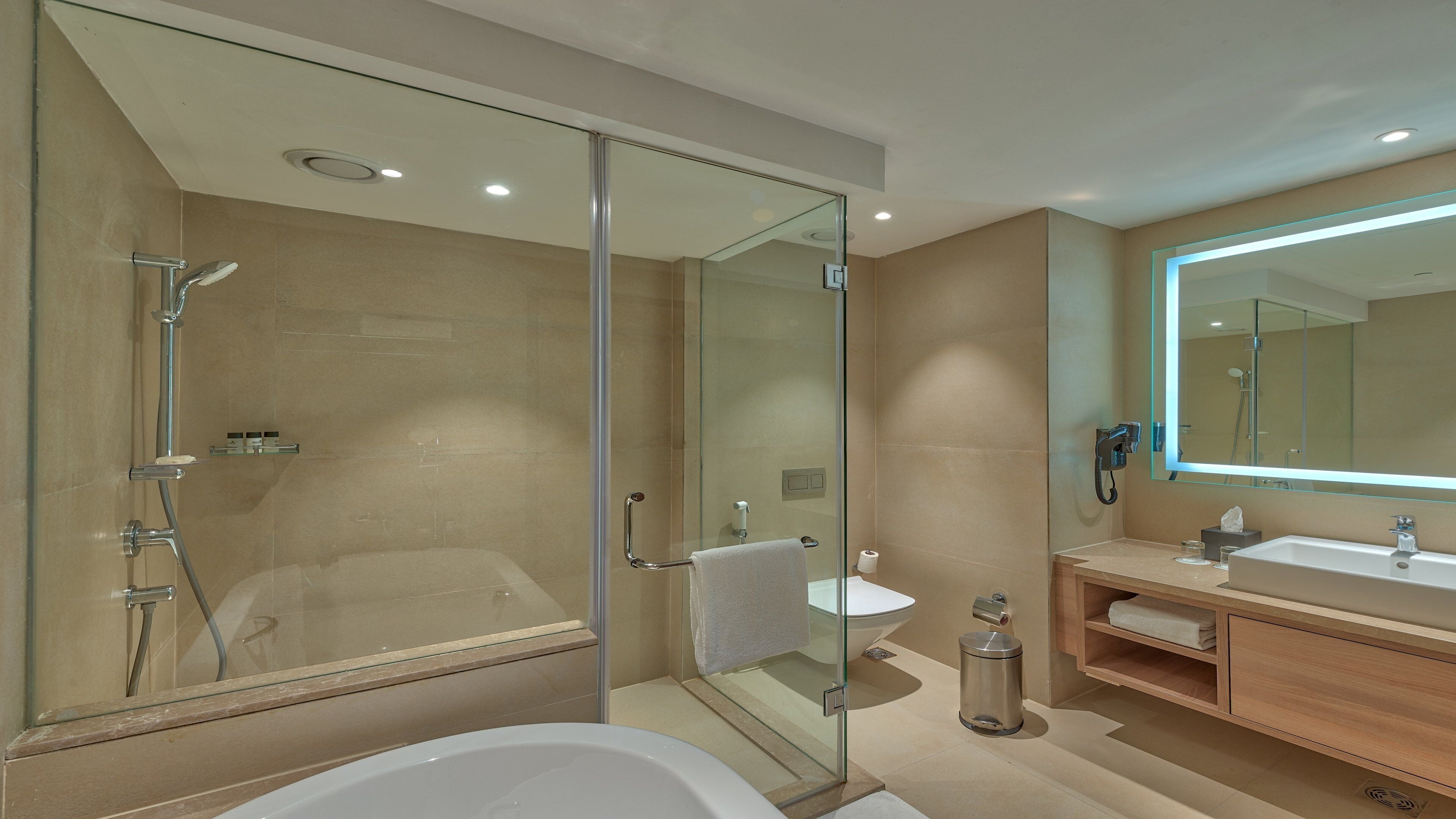 Une salle de bain moderne dotée d’une douche à parois de verre, d’une baignoire, d’un grand miroir et d’un meuble-lavabo avec un évier.