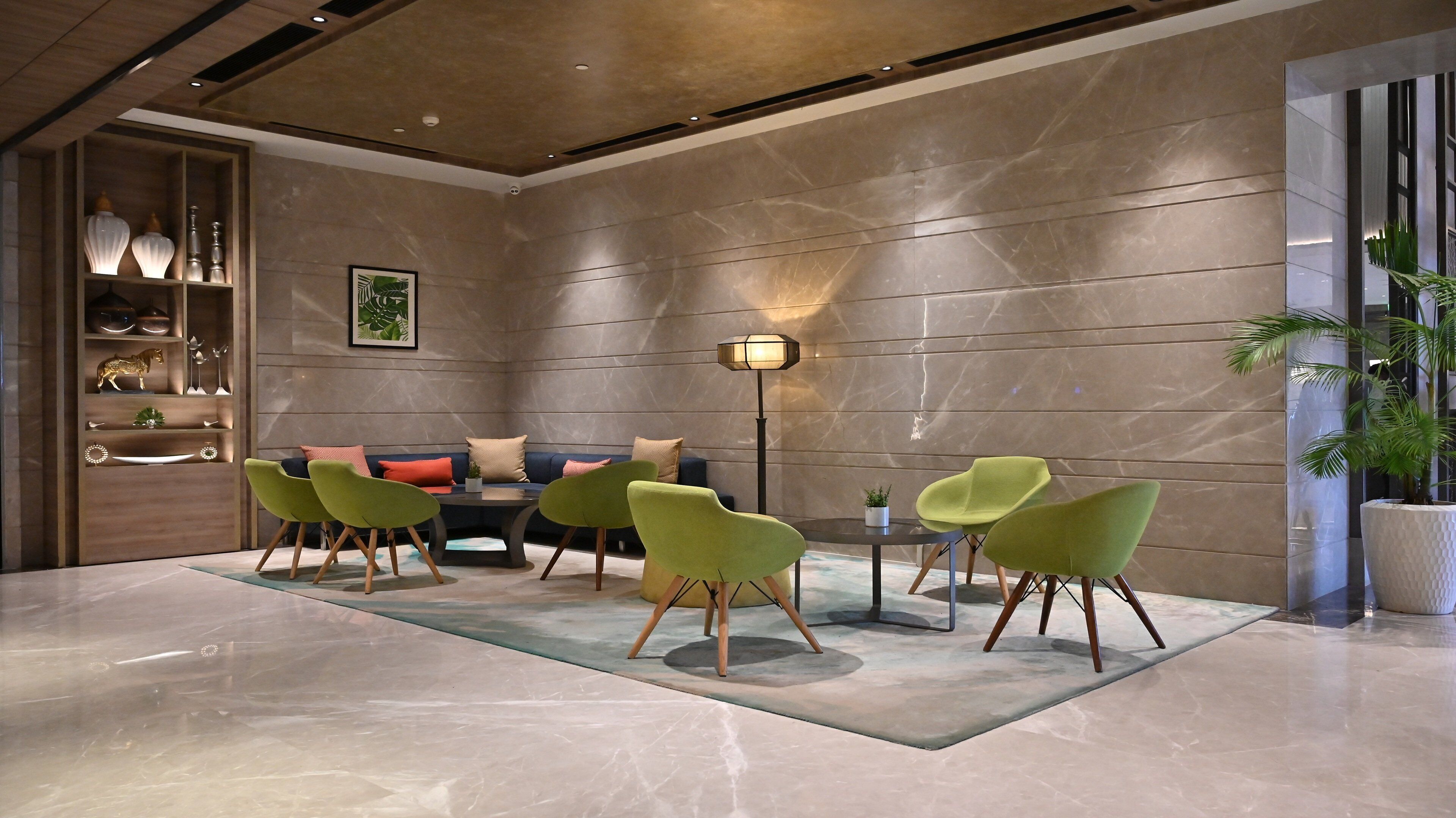 A modern lobby with a marble floor, a sofa set, green chairs, a floor lamp, and a plant.