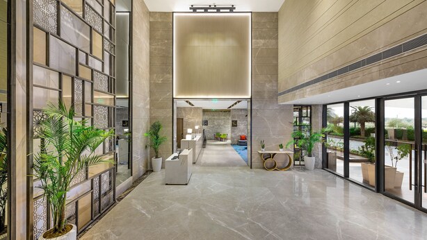 Um hall amplo com teto alto, piso de mármore e mobiliário moderno. Há plantas em vasos e uma área de estar com vista para o exterior.