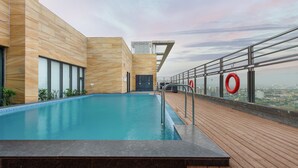 Uma piscina no terraço com um deck de madeira, vista da cidade e um edifício moderno com fachada estampada.