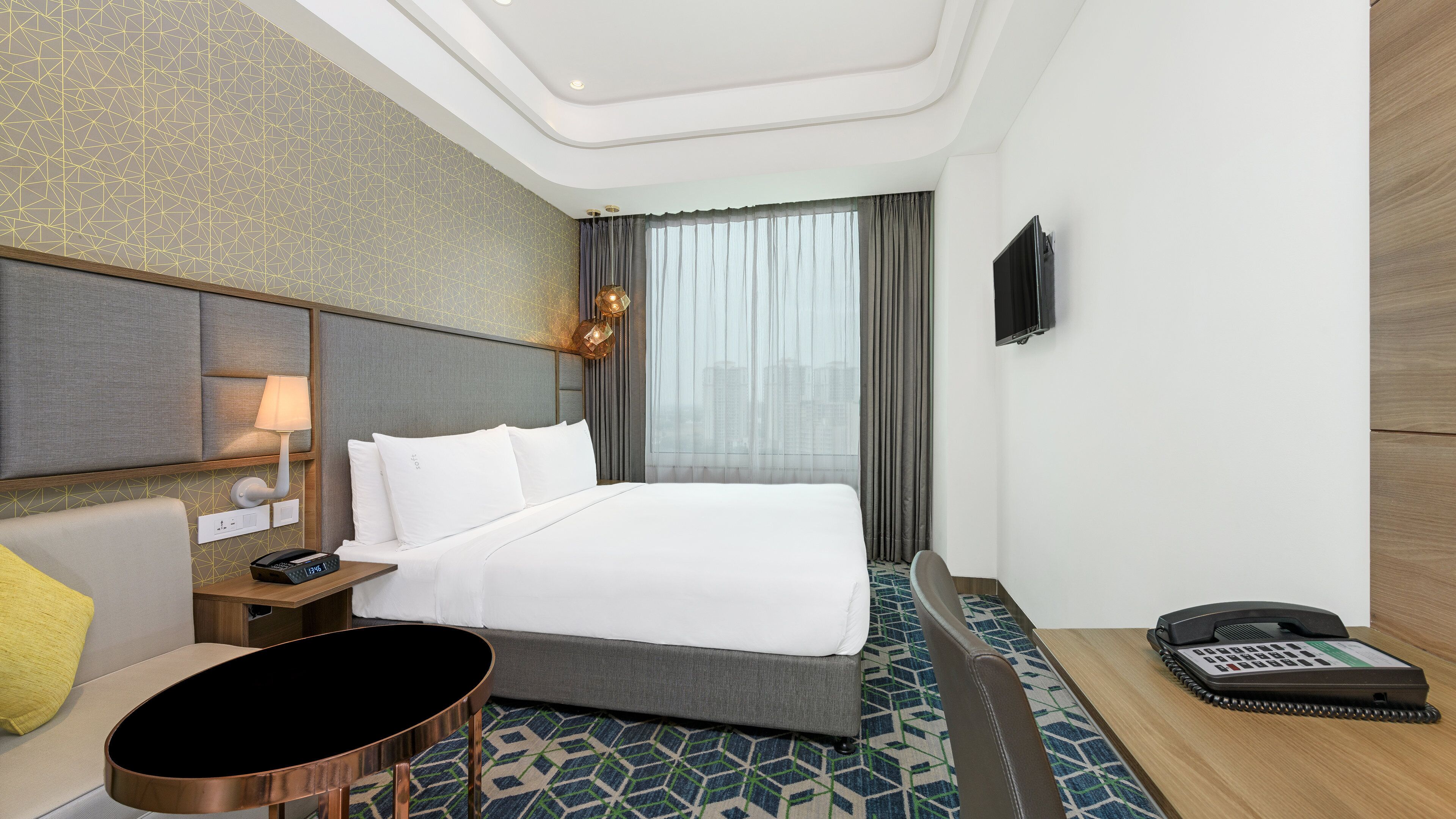 A hotel room with a bed, bedside table, lamp, and a phone on the side table.