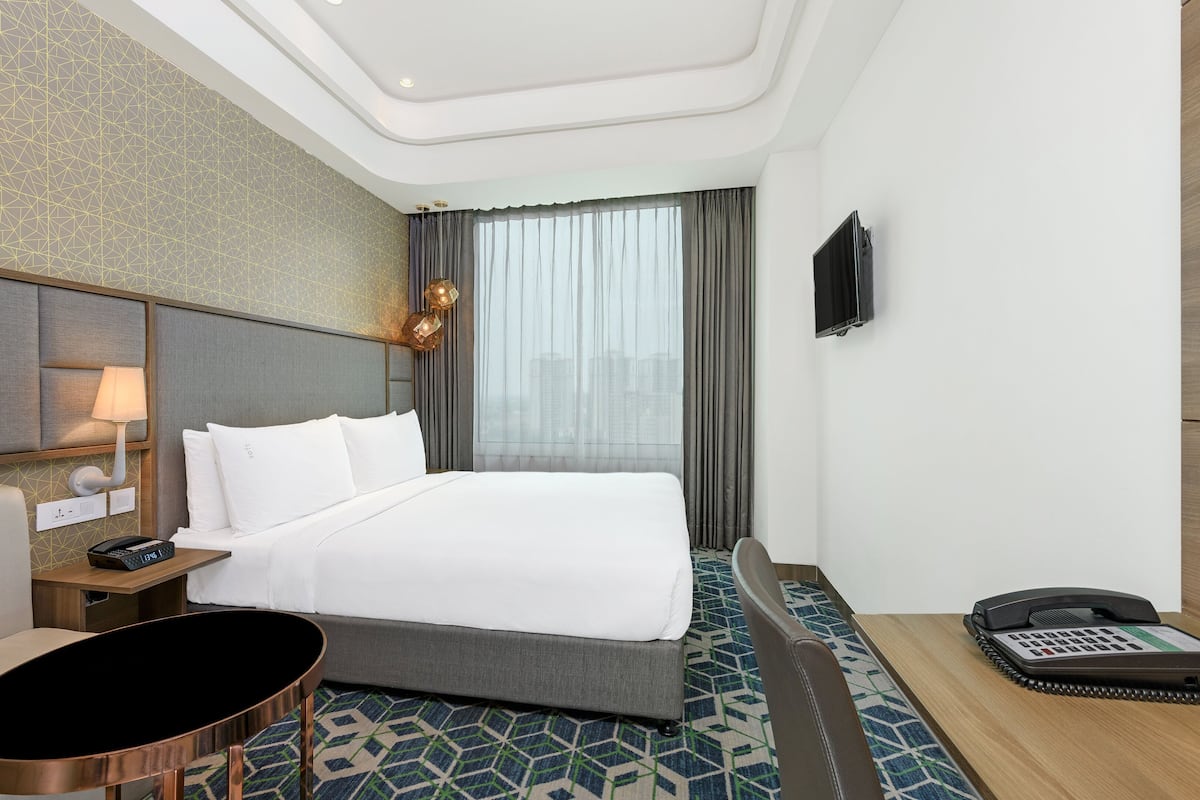 A hotel room with a bed, bedside table, lamp, and a phone on the side table.