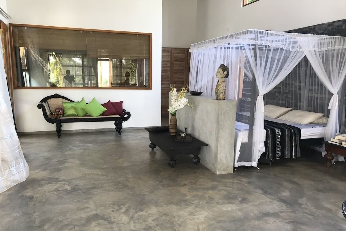 Una habitación con un espejo grande, una cama con dosel, una mesita con adornos y un banco con cojines.