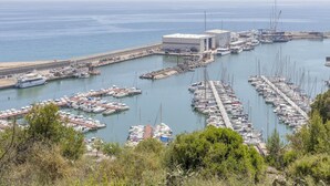 Un port de plaisance où sont amarrés de nombreux bateaux, un grand bâtiment et une plage en arrière-plan.