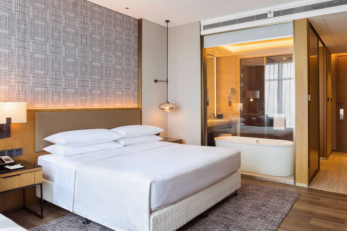 Ein modernes Hotelzimmer mit einem großen Bett, Nachttisch und einem Badezimmer mit Badewanne und Duschkabine.