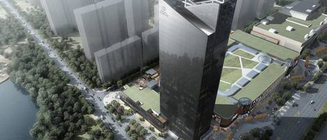 Un immeuble moderne de grande hauteur, doté d’un sommet triangulaire original, entouré d’un espace paysager agrémenté d’arbres et bordé d’une route.