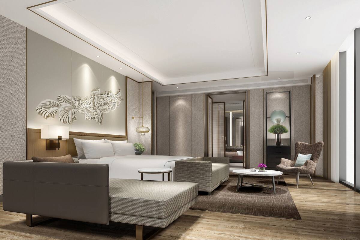 Ein modernes Hotelzimmer mit einem großen Bett, einer Couch, einem kleinen Tisch und einem Sessel. Es gibt einen Spiegel, eine Lampe und eine Wanddekoration.