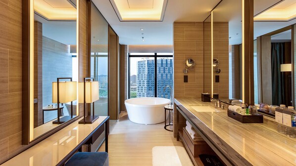 A modern bathroom with a large bathtub, a vanity with a mirror, and a view of the cityscape.