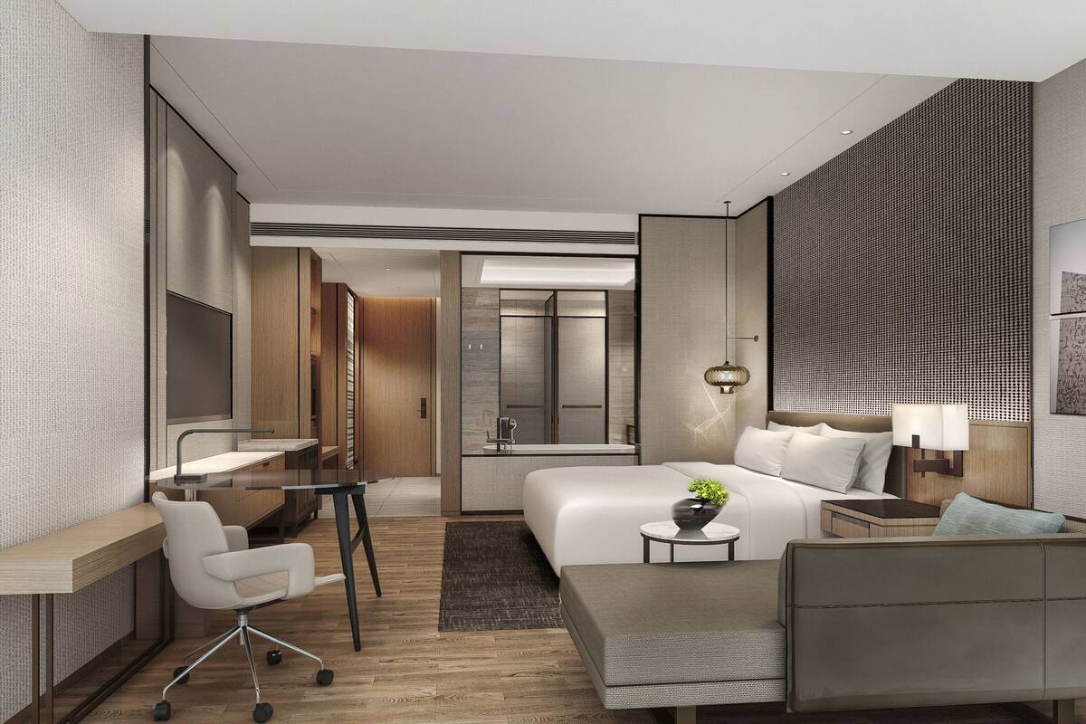 Ein modernes Hotelzimmer mit einem großen Bett, einem Schreibtisch, einem Sessel und einem kleinen Tisch mit einer Pflanze.