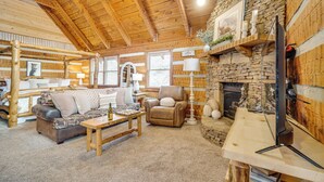 A cozy log cabin interior with a stone fireplace, wooden furniture, and a television. - Honey Bear Pause: Rural Escape w/ Porch & Hot Tub! (Townsend)