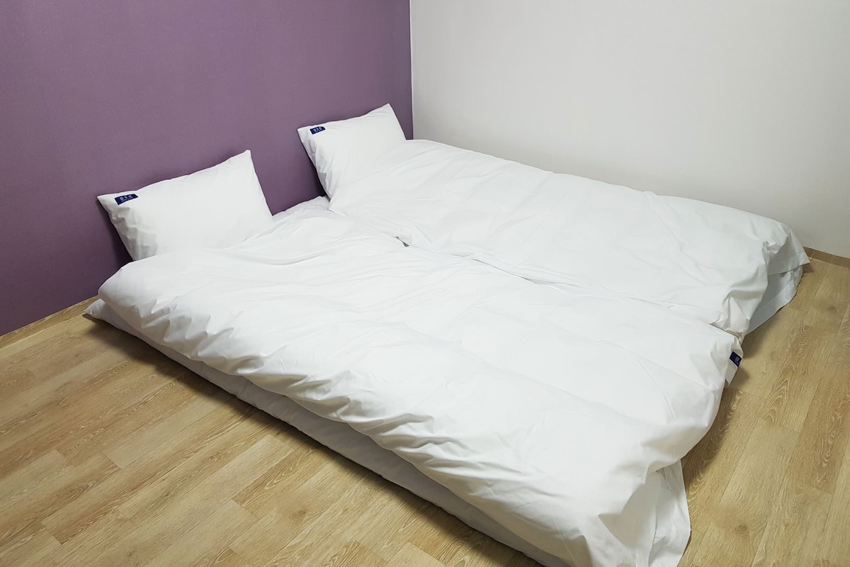 Una cama individual con ropa de cama blanca en una habitación con paredes moradas y blancas y suelo de madera.