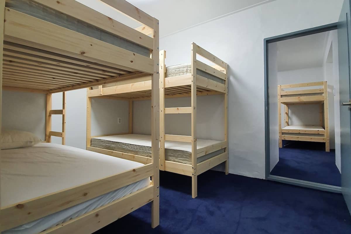 Una habitación con tres literas, una lámpara en el techo y una puerta que da a otra estancia.