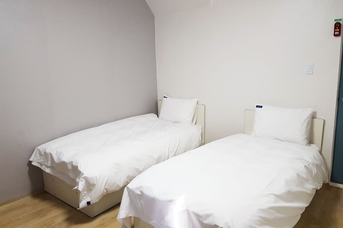 Una habitación con dos camas individuales, ropa de cama blanca, suelo de madera y una pared blanca lisa.