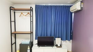 A room with a white desk, a black TV, a shelf with hangers, a small heater, and a blue curtain. - Bluemoon Guest House - Hostel (Taebaek)