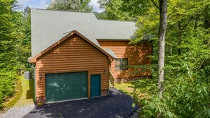 Surrounded by lush greenery, this cabin features a sloped roof and a prominent garage door.