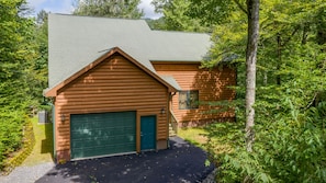 Surrounded by lush greenery, this cabin features a sloped roof and a prominent garage door.