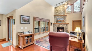 Relax in this inviting living room with a stone fireplace, comfortable armchair, and large window offering a view of the outdoors.