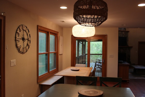 Enjoy meals in this dining area with a table and chairs, a wall-mounted clock, and a hanging light fixture, offering a view of the outdoors through large windows.