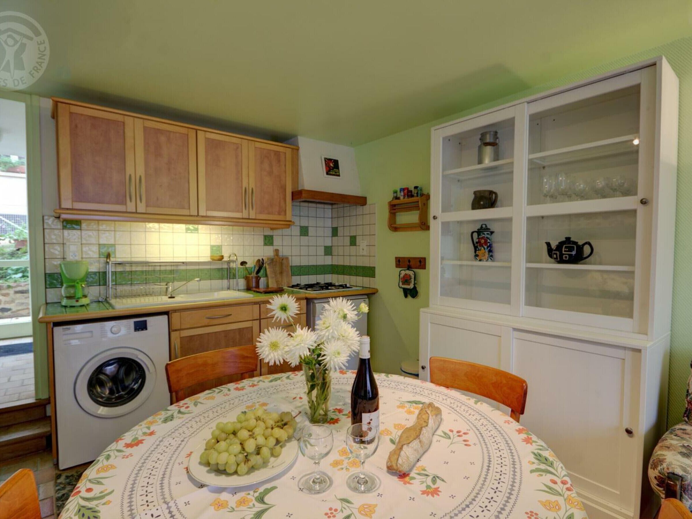 Una cocina con armarios de madera, lavadora, lavaplatos y comedor con mesa dispuesta para dos.