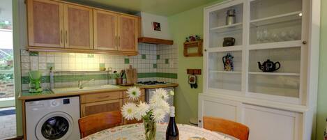 Una cocina con armarios de madera, lavadora, lavaplatos y comedor con mesa dispuesta para dos.