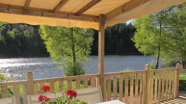 Een overdekt terras met uitzicht op een meer en bomen.