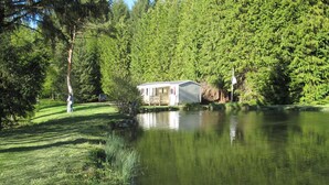 Een klein huisje aan een vijver, omringd door bomen.