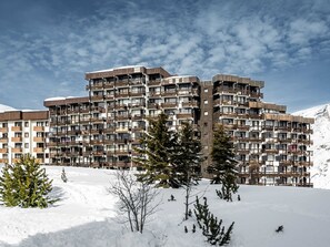 Ein mehrstöckiges Hotel mit Balkonen vor einer verschneiten Berglandschaft.