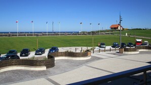 A parking area with cars, a grassy field, and flags in the background.