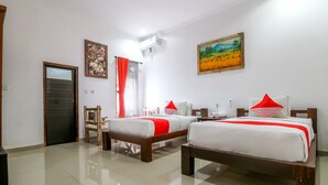 Une chambre d’hôtel avec deux lits, une porte en bois, un tableau et un appareil de climatisation.
