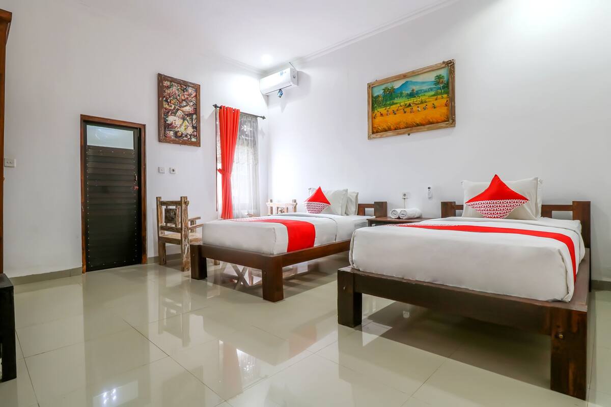 A hotel room with two beds, a wooden door, a painting, and an air conditioning unit.