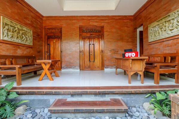 A room with wooden furniture, a stone-tiled floor, and a central door with intricate carvings. - OYO 2607 Men Bebas Residence (Ubud)