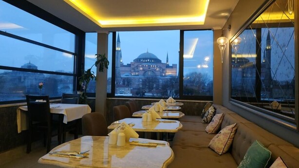 A restaurant with tables set for dining, a sofa, and large windows offering a view of a historic building. - Basilica GuestHouse (Istanbul)